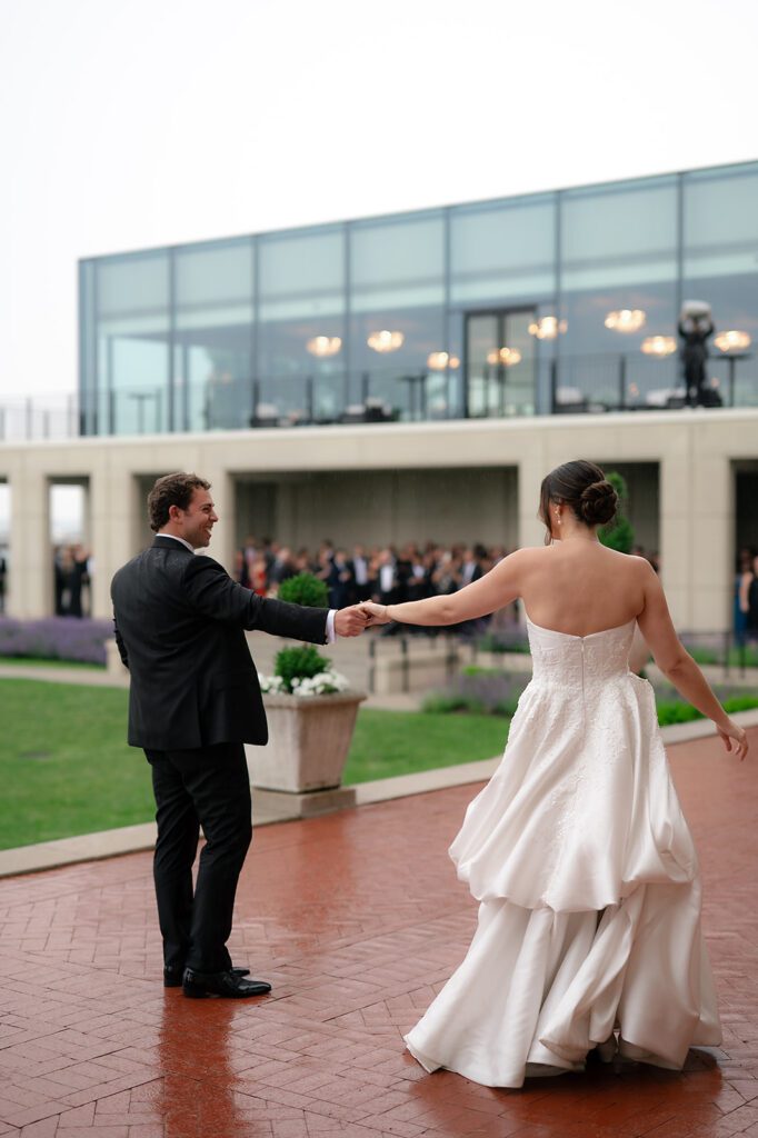 Bride and groom sharing their first dance outdoors while guests watch from the patio at Grosse Pointe War Memorial during cocktail hour.
