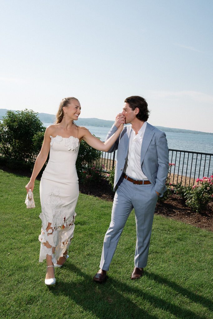 Bride and groom walking hand in hand along the waterfront during their Delamar welcome party in Traverse City, Michigan.