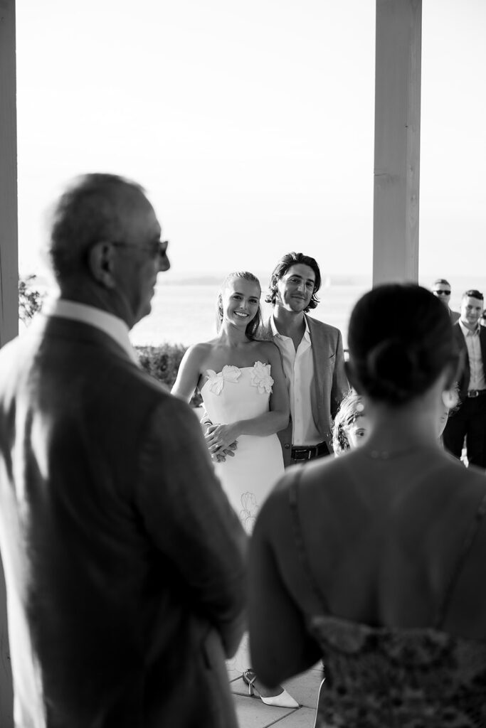 Black and white photo of the bride and groom smiling during speeches at a welcome wedding party at The Delemar in Traverse City, Michigan.