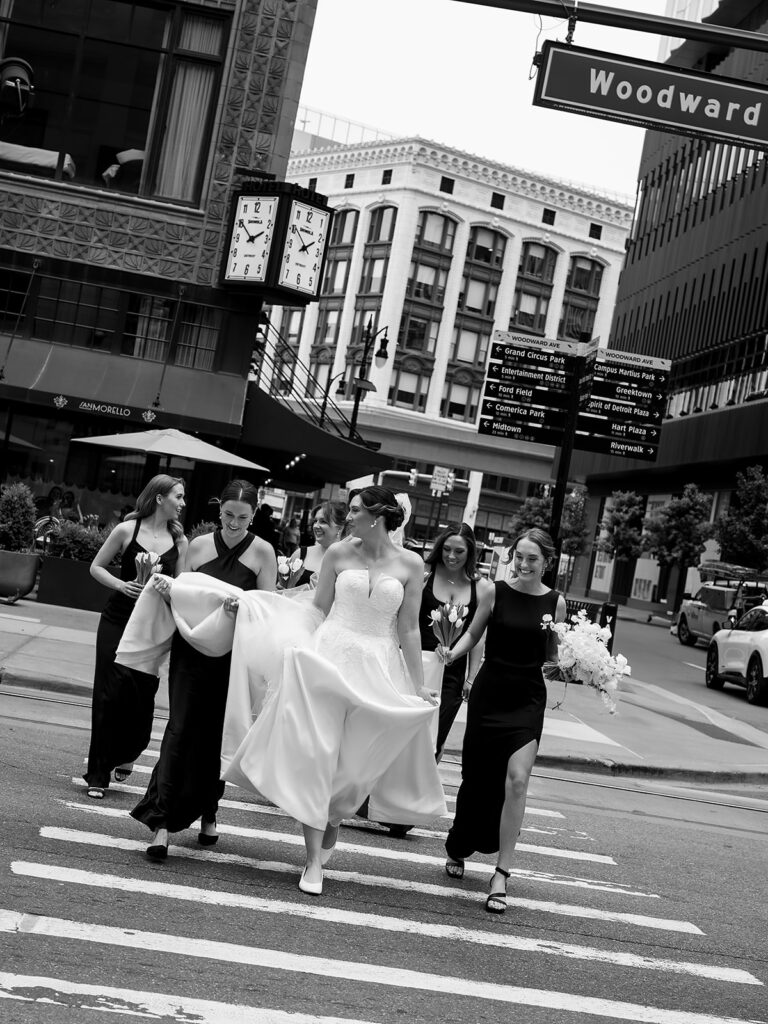 Bride walking with her bridesmaids across Woodward Avenue during downtown Detroit wedding portraits.
