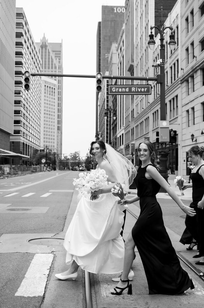 Bride and bridesmaid crossing Grand River Street for downtown Detroit wedding portraits before the ceremony.
