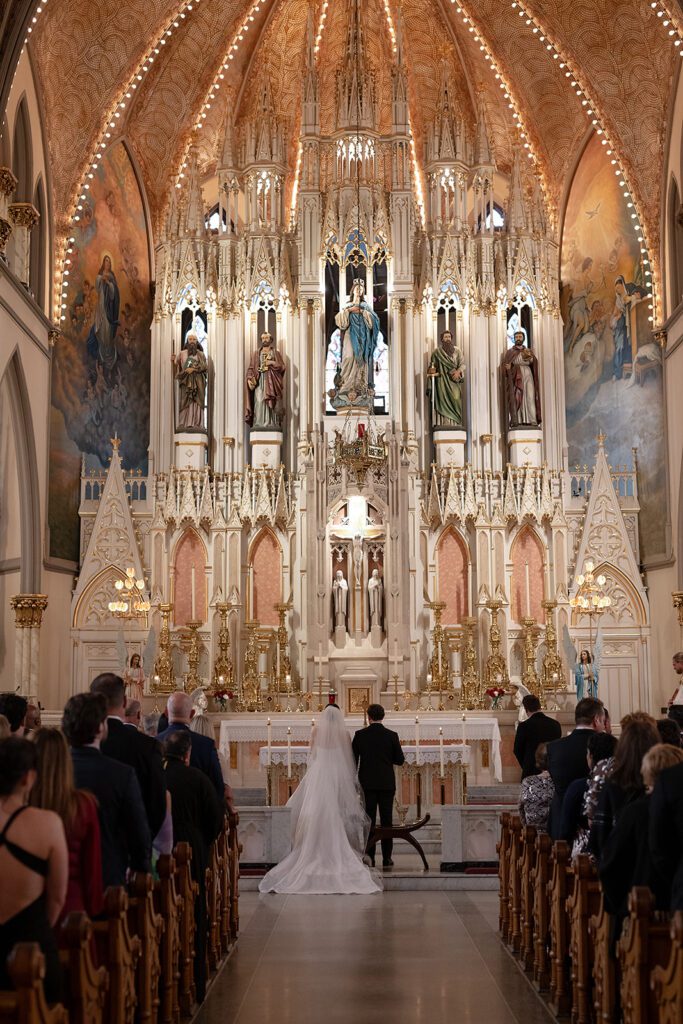 Couple standing at the altar surrounded by ornate architecture at Sweetest Heart of Mary Church.