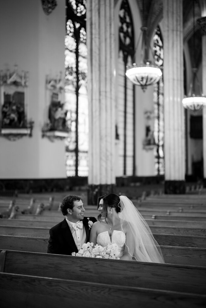 Black and white photo of the bride and groom sitting in the church pews at Sweetest Heart of Mary Church in Detroit.