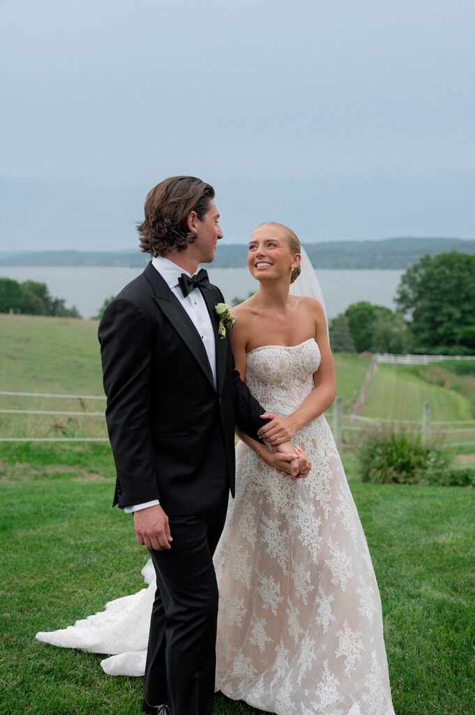 Bride and groom walk across the rolling hills of Noverr Farms with Lake Leelanau in the distance.