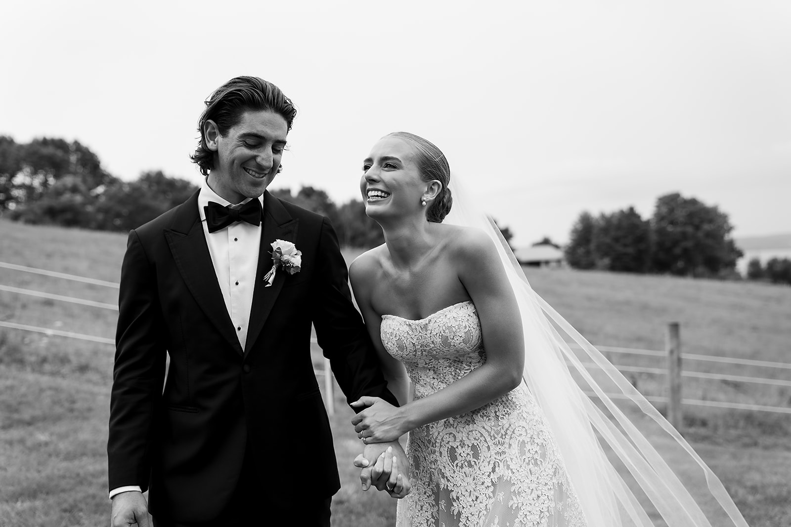 Bride and groom laugh together during relaxed wedding portraits with Lake Leelanau behind them.