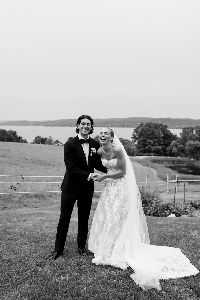 Black and white candid photo of the bride and groom laughing during their Traverse City wedding portraits at Noverr Farms.