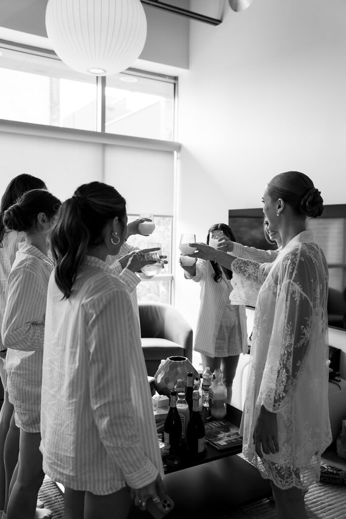 Black and white photo of the bride and bridesmaids toasting with mimosas.