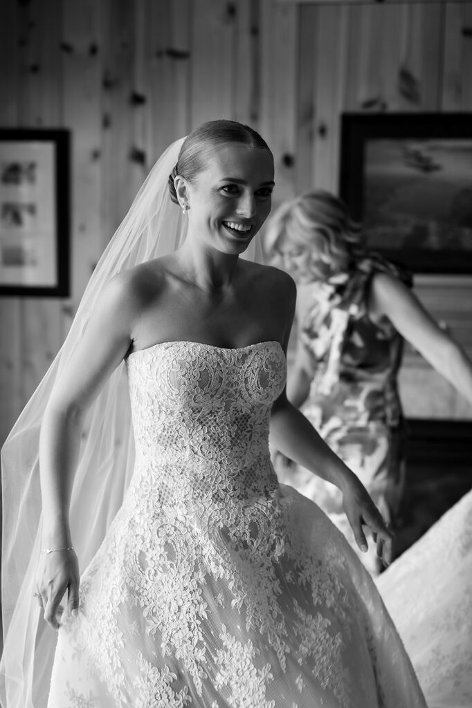 Bride wearing her veil and wedding gown, smiling as final touches are finished.