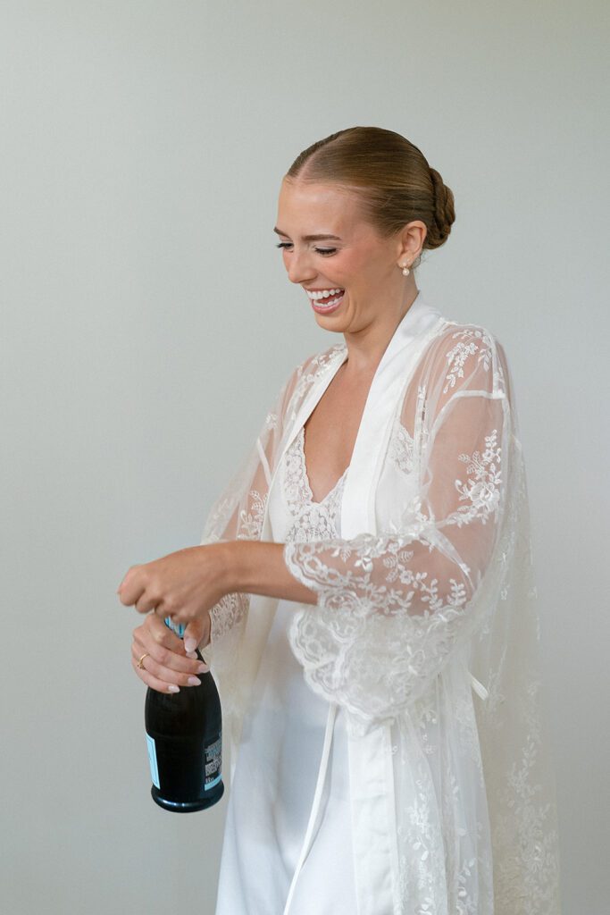 Candid photo of a bride laughing while opening a bottle of champgagne.