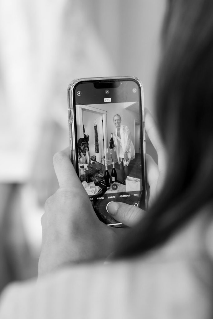 Black and white photo of someone taking an iPhone photo of the bride