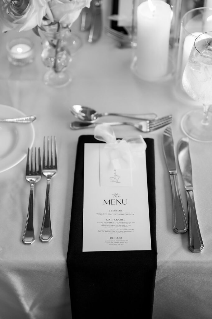 Close-up of a wedding place setting with printed menu card, black linen napkin, and elegant tableware at a Grosse Pointe War Memorial reception.