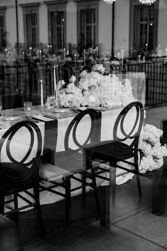 Black and white detail photo of a wedding reception table with lush white floral centerpieces and modern black chairs at Grosse Pointe War Memorial.