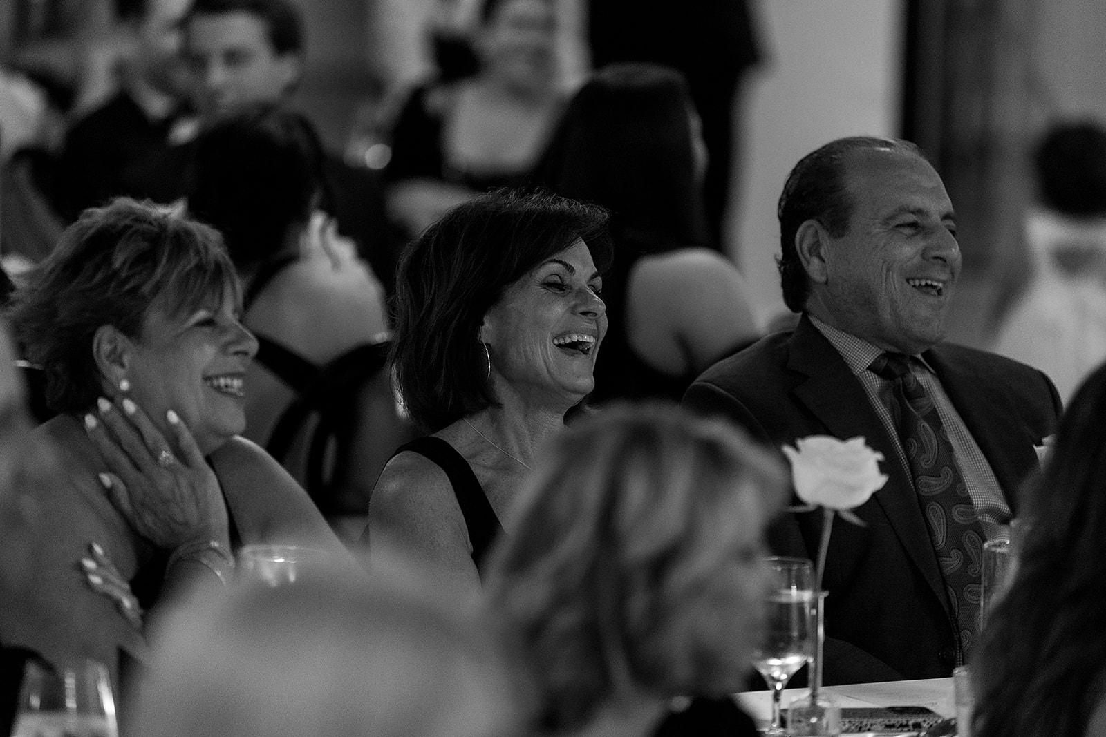 Black and white wide shot of guests laughing during speeches.