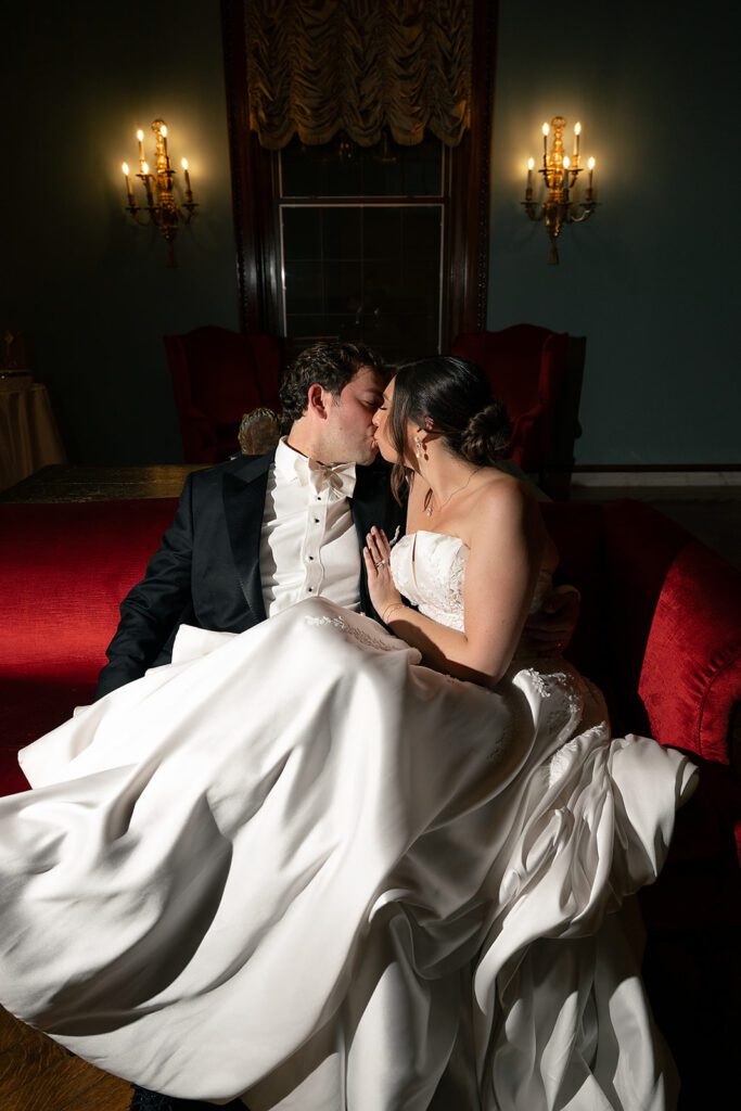 Bride and groom kissing on a loveseat during their Grosse Pointe War Memorial wedding reception.
