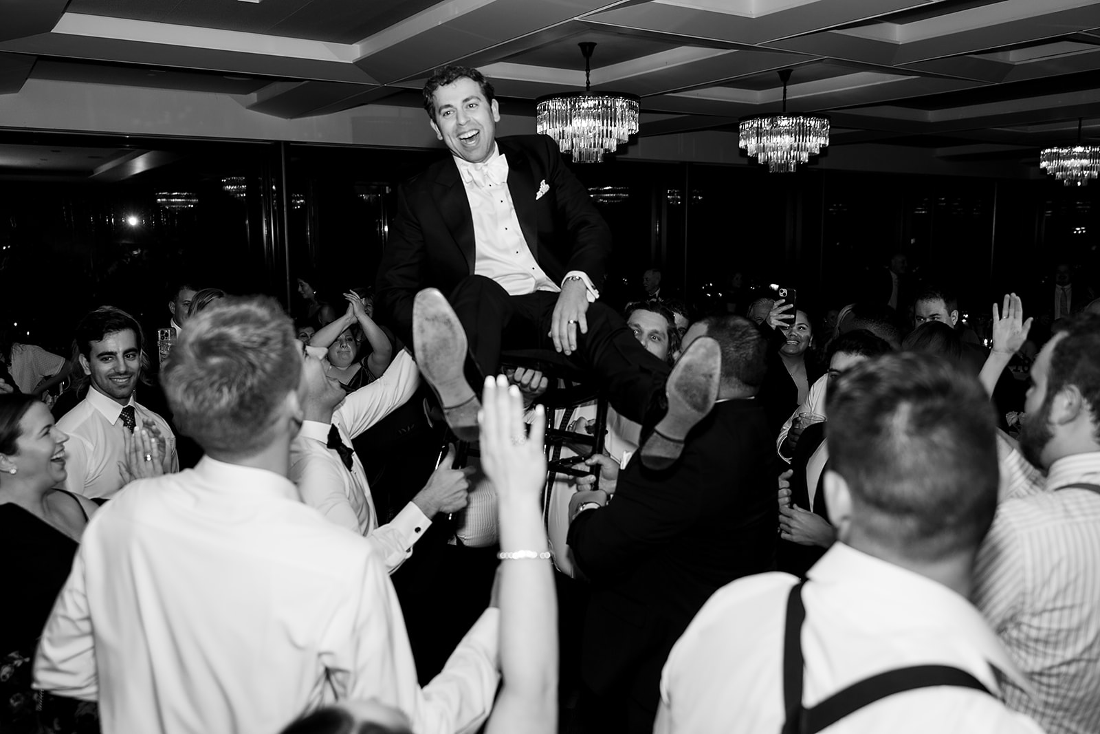 Black and white photo of the groom being lifted in the air on a chair.