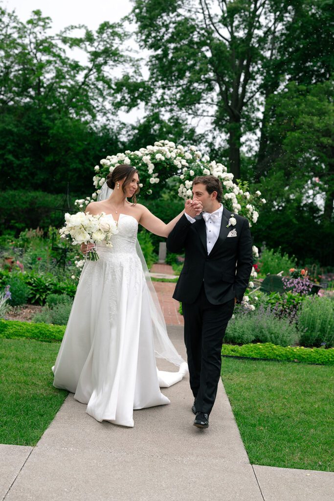Bride and groom walking in front of a a floral arch at The War Memorial.