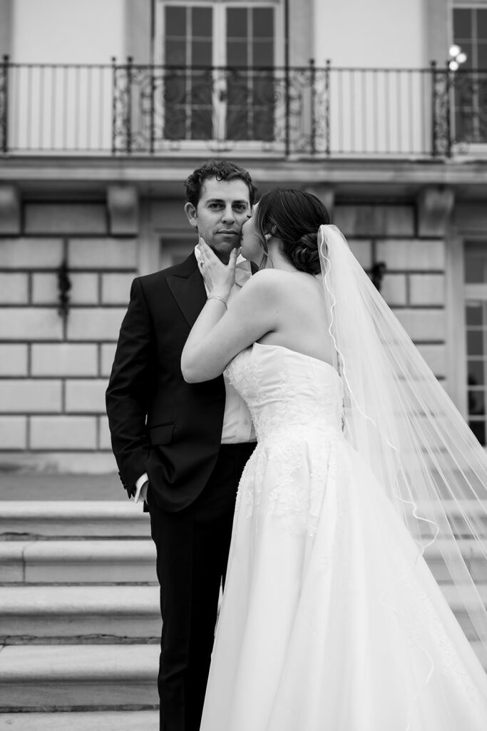Black and white wedding portrait of a bride kissing the groom on the steps of The War Memorial in Grosse Pointe Farms.
