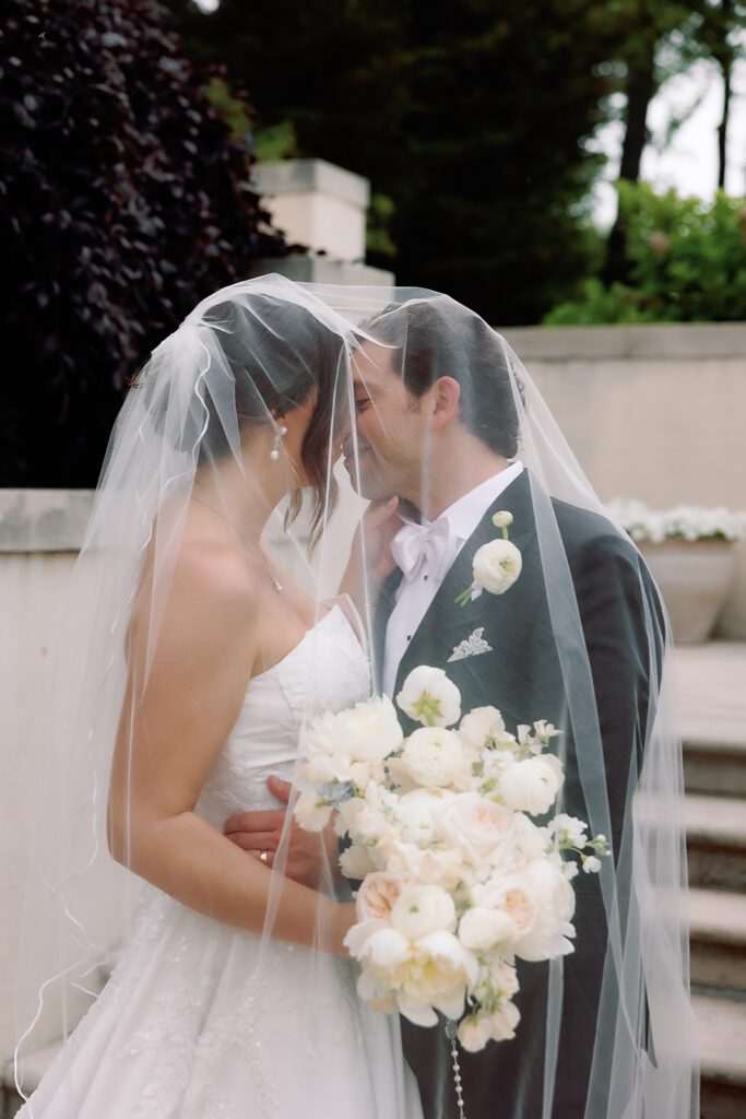 Bride and groom kissing underneath the brides veil for portraits. 