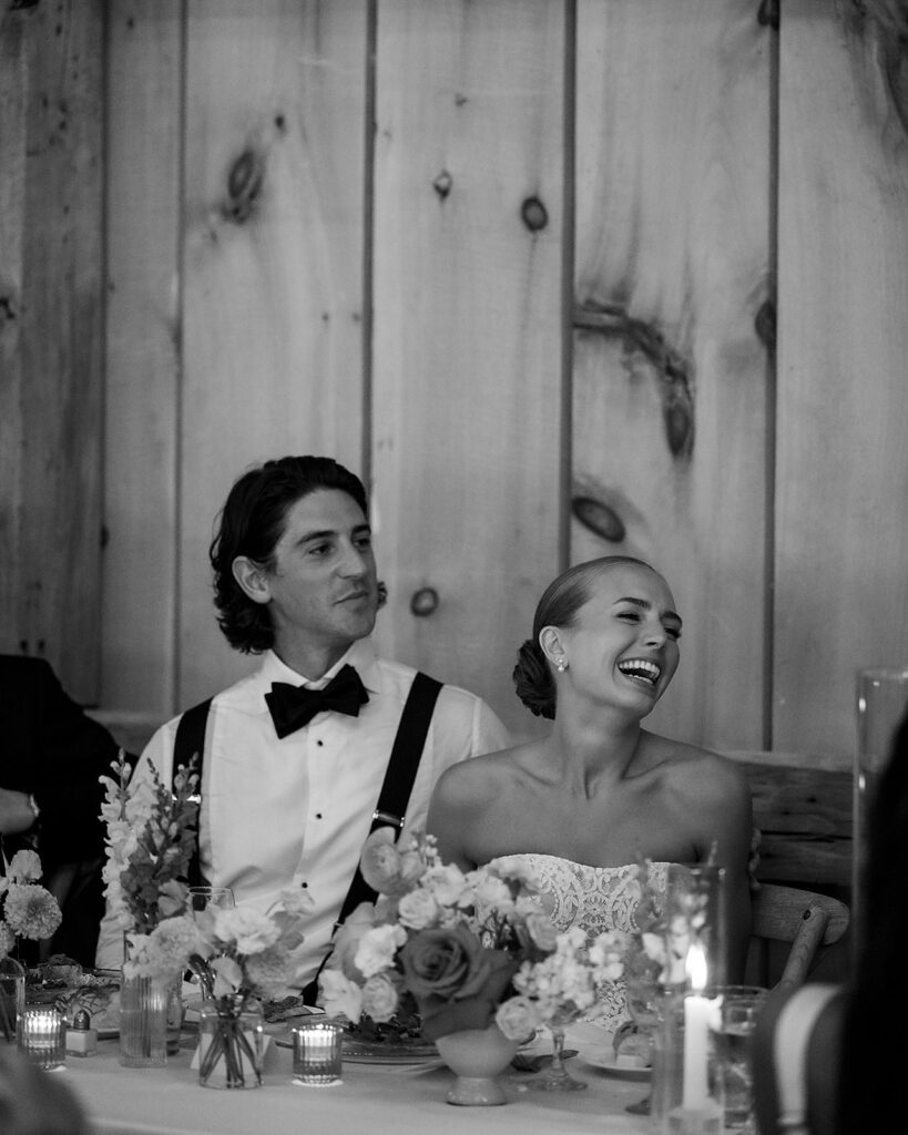 Bride and groom laughing together at the head table during their Noverr Farms wedding reception in Traverse City, Michigan.