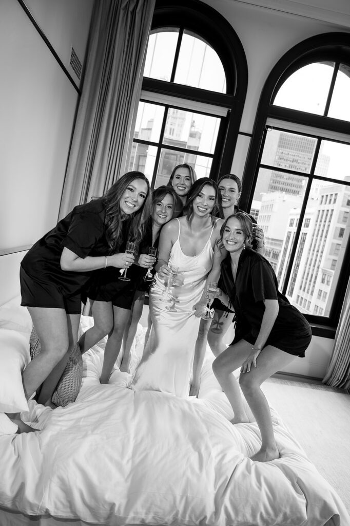 Bride and bridesmaids celebrating together on the bed at the Shinola Hotel in Detroit.