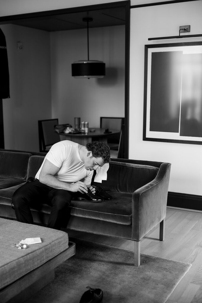 Groom tying his shoes while getting ready on a velvet sofa at the Shinola Hotel in Detroit.