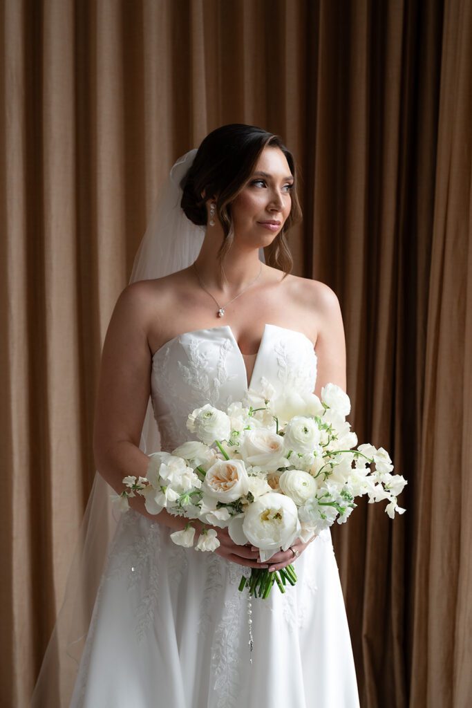 Bride standing by the window holding her bouquet during getting ready at the Shinola Hotel.
