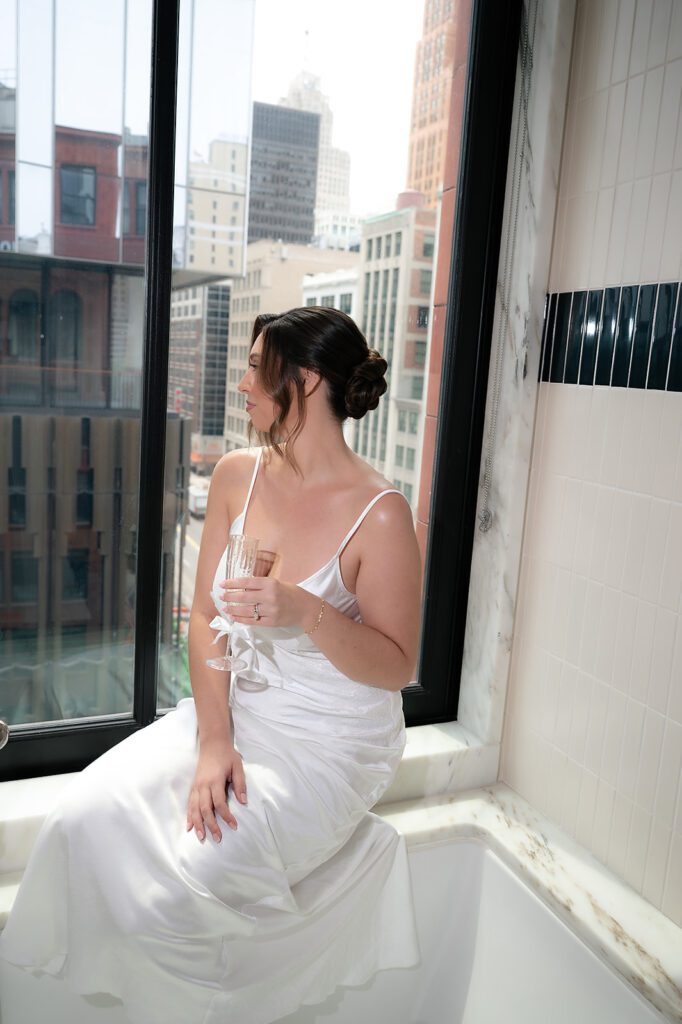Bride sitting by the window with champagne during Shinola Hotel wedding getting ready.