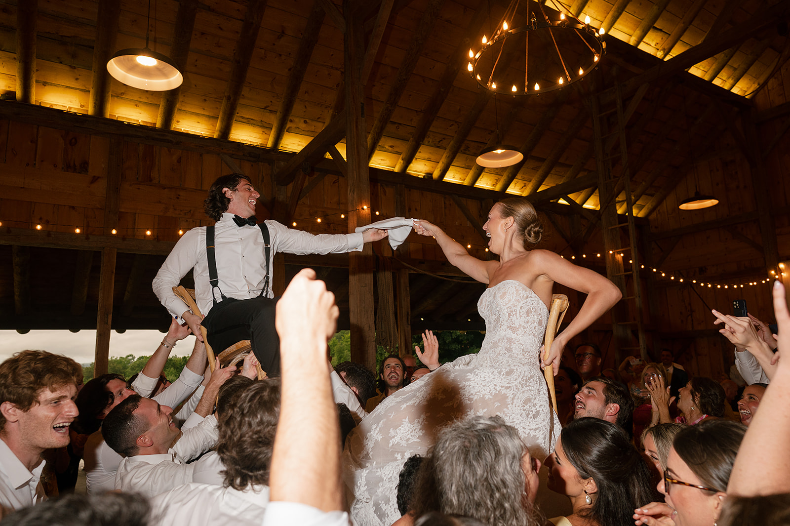 Bride and groom being lifted in the air on chairs during their reception.