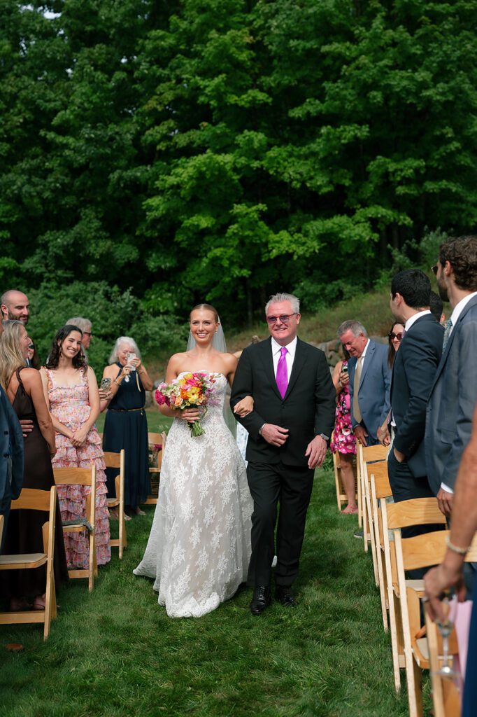Bride walks down the aisle with her father during an outdoor Noverr Farms wedding ceremony in Traverse City.