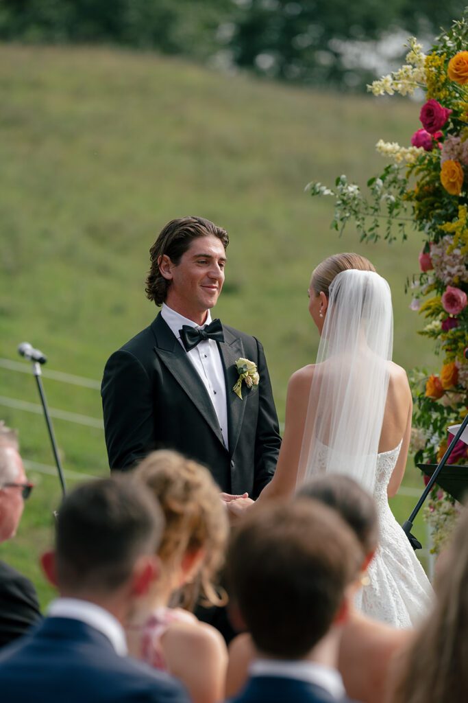 Groom smiles at the bride during their vows at an outdoor Traverse City wedding ceremony at Noverr Farms.