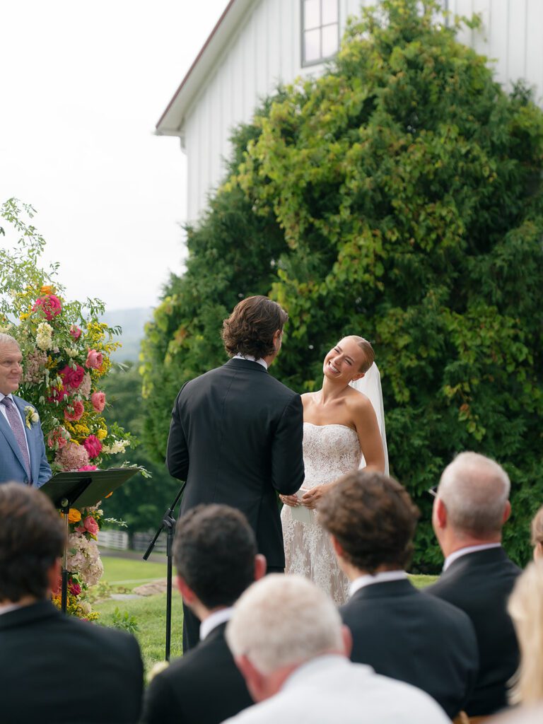 Bride laughs during her wedding ceremony at Noverr Farms with colorful florals framing the altar.