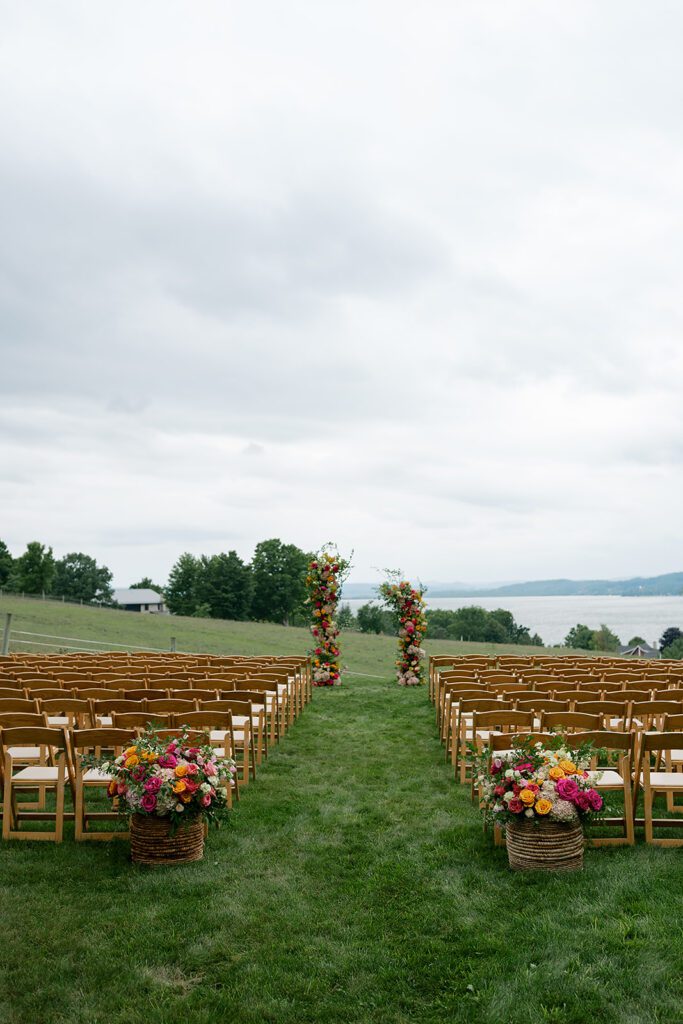 Outdoor ceremony setup at Noverr Farms in Traverse City, Michigan, with wooden chairs, colorful florals, and Lake Leelanau in the distance.