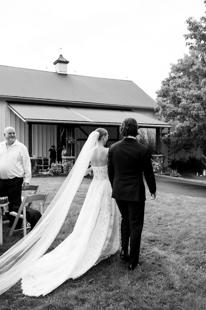 Black and white photo of a bride and groom walking back to Noverr Farms after their wedding ceremony.