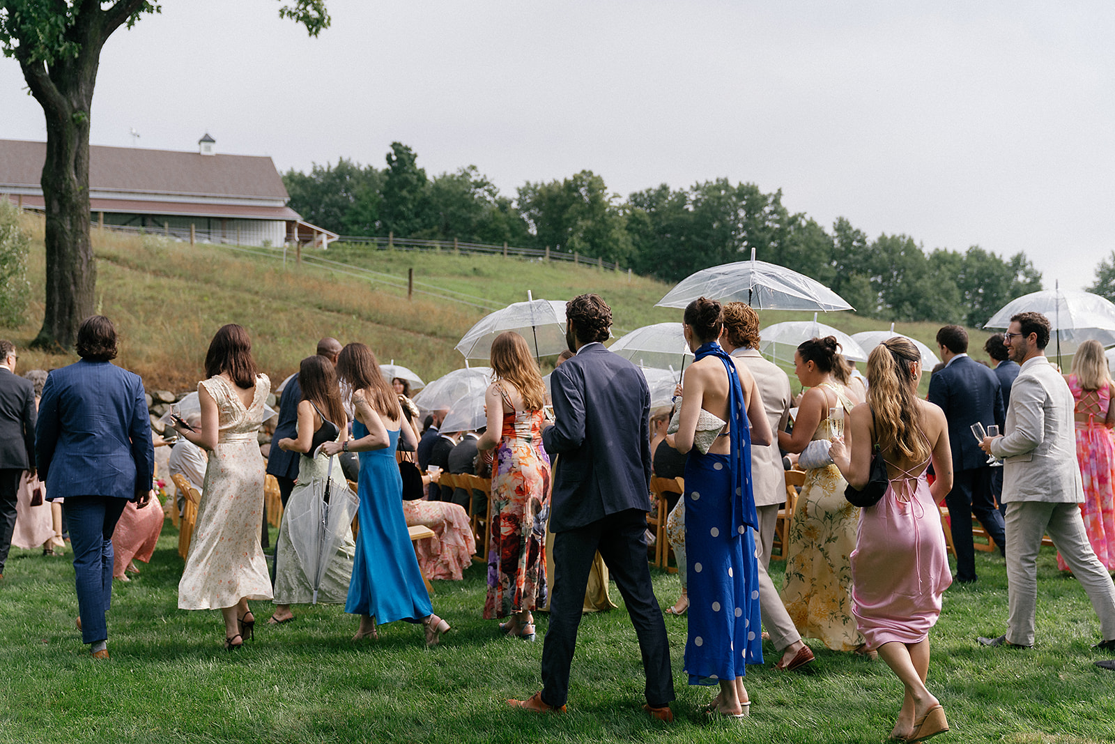 Wedding guests walk toward the ceremony site at Noverr Farms holding clear umbrellas in Northern Michigan.