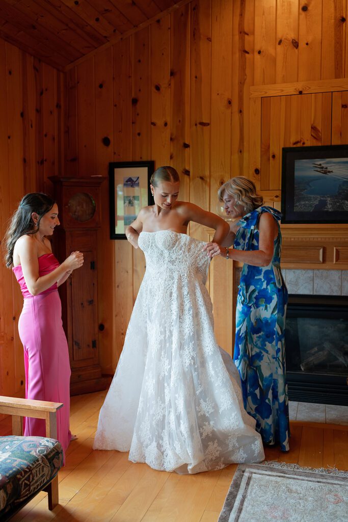 Candid photo of a bridesmaids and the brides mother helping her get into her wedding dress.