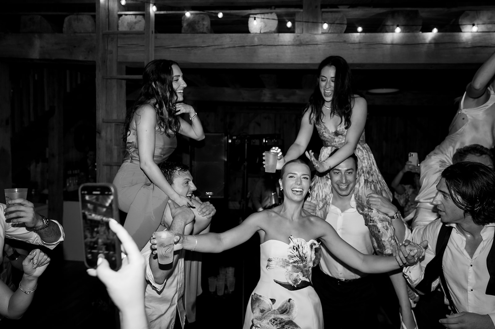 Black and white candid wedding reception photo of a bride dancing with her friends.